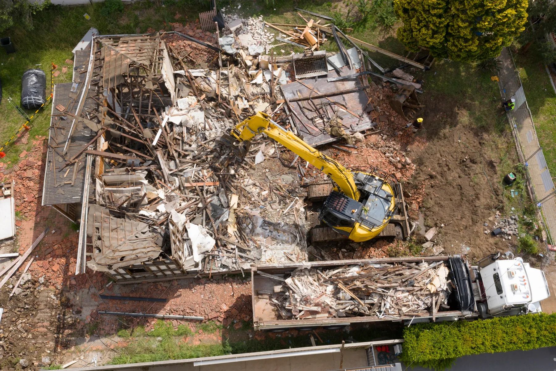 Aerial view of a structure being demolished with an excavator and a loaded haul truck