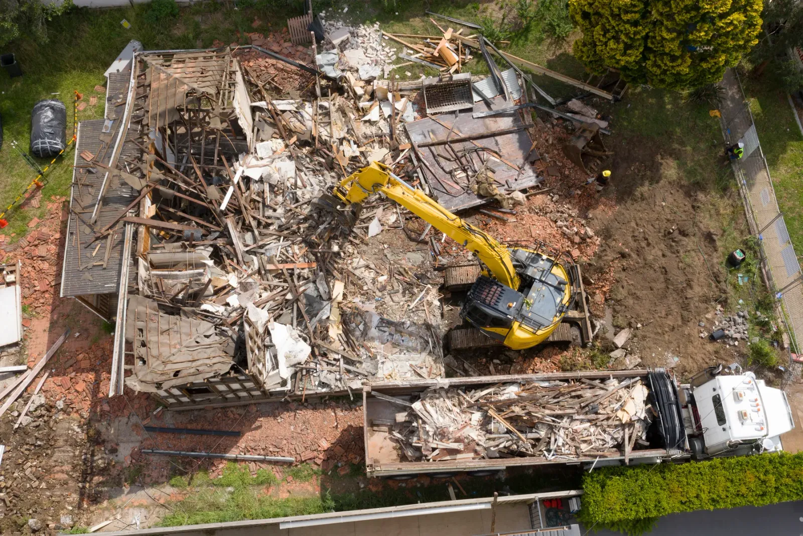 Aerial view of a structure being demolished with an excavator and a loaded haul truck