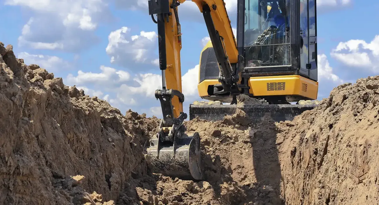 Excavator digging and shaping a broad earthwork cut