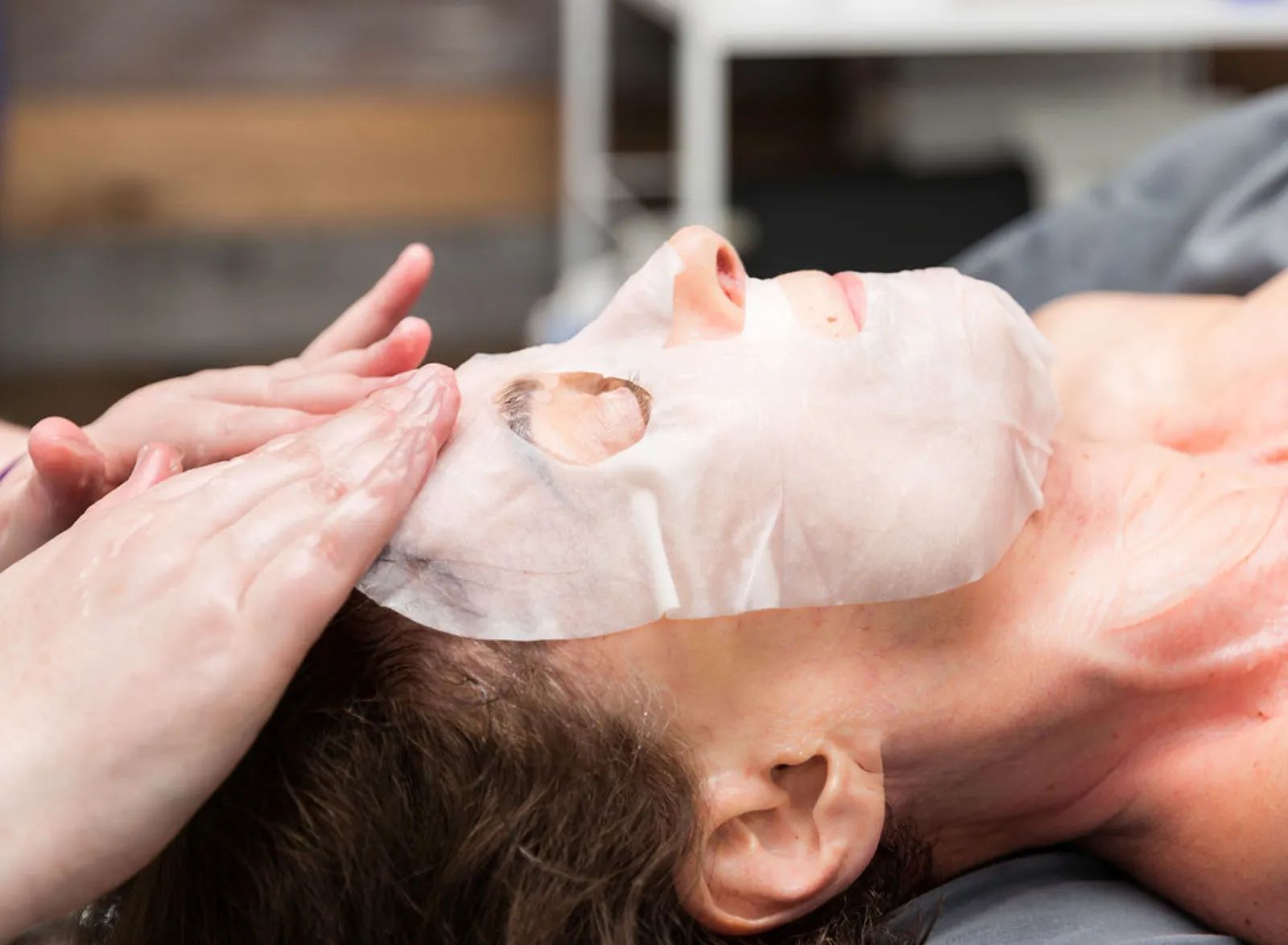 Hands applying a sheet mask during a facial at Piedmont Injury Massage in Hoschton, GA