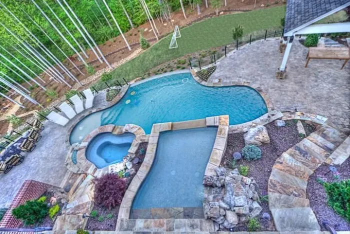 Freeform swimming pool, raised spa, and stone patio viewed from above