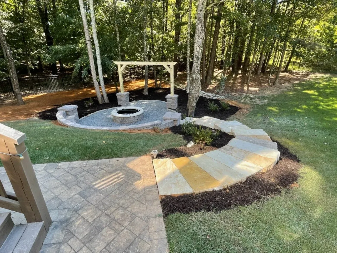 Curved stone steps leading to a fire pit and pergola in a wooded backyard