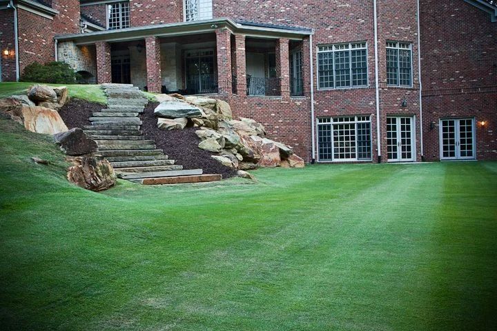 Broad stone steps and boulders connecting a green lawn to the house