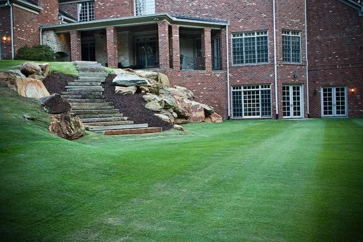 Broad stone steps and boulders connecting a green lawn to the house