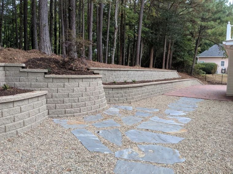 Tiered block retaining walls and stone paving beside a wooded hillside