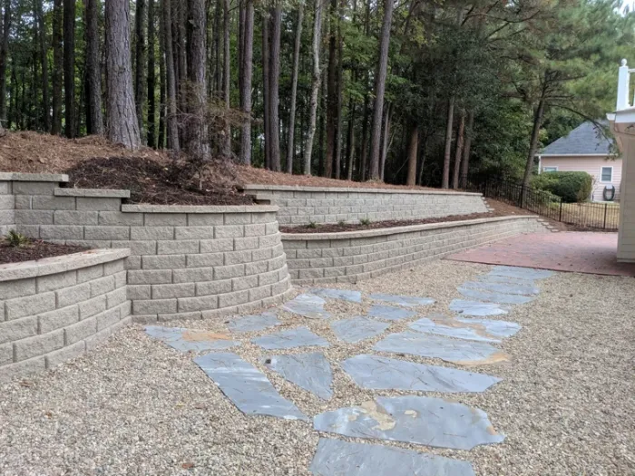 Tiered block retaining walls and stone paving beside a wooded hillside
