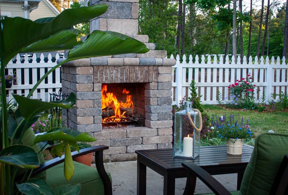 Outdoor fireplace with green lounge chairs and flowering pots