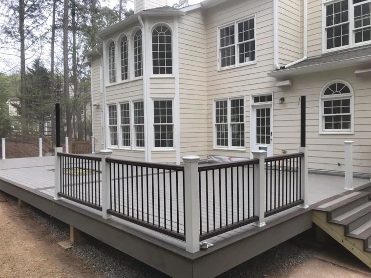 Large composite deck with black railings beside a white home