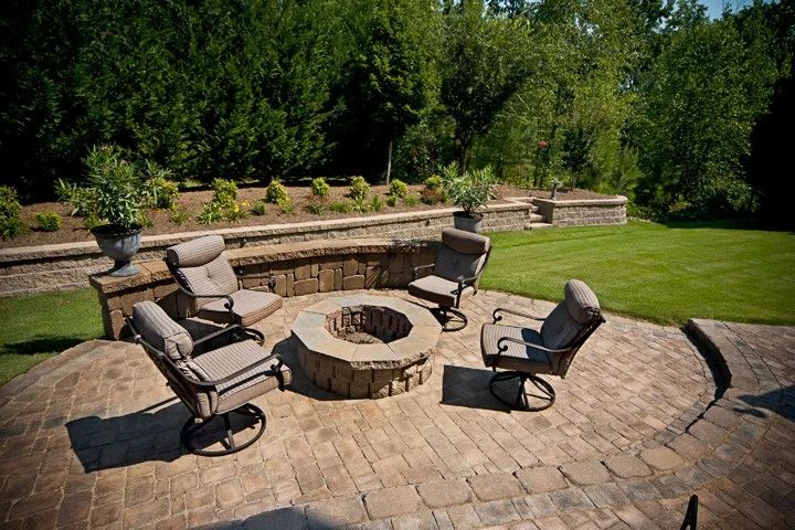 Circular paver patio with a stone fire pit, lounge chairs, and a seating wall