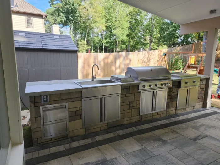 Covered outdoor kitchen with stainless steel grill, sink, and storage