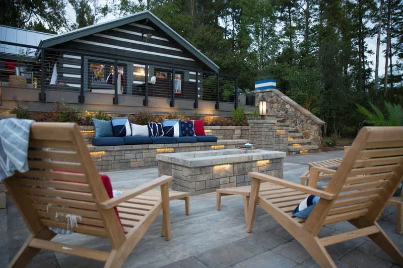 Furnished stone patio with a fire pit and pavilion beside a lake