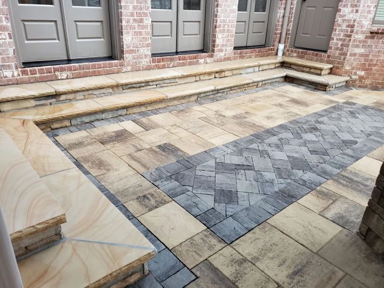 Patterned paver patio and broad stone steps beside a brick home