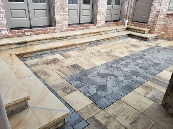 Patterned paver patio and broad stone steps beside a brick home