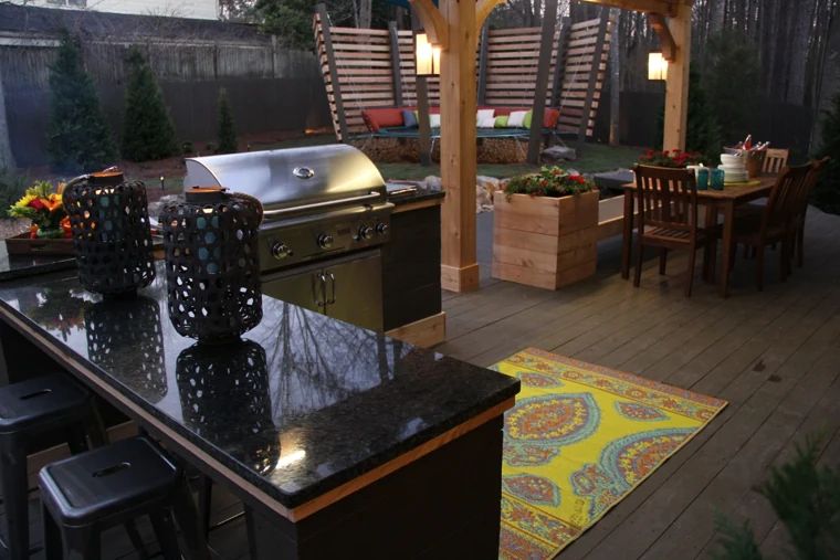 Outdoor kitchen with a stainless steel grill and dark countertop beneath a pergola