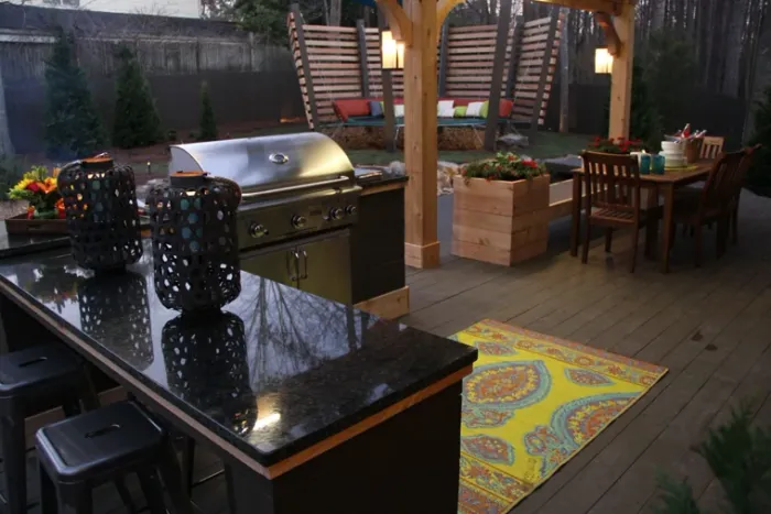 Outdoor kitchen with a stainless steel grill and dark countertop beneath a pergola