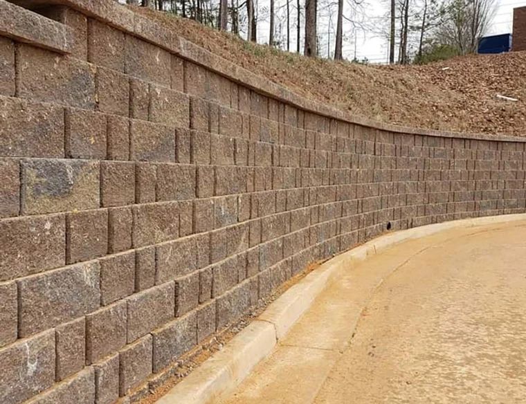 Curved block retaining wall supporting a wooded hillside