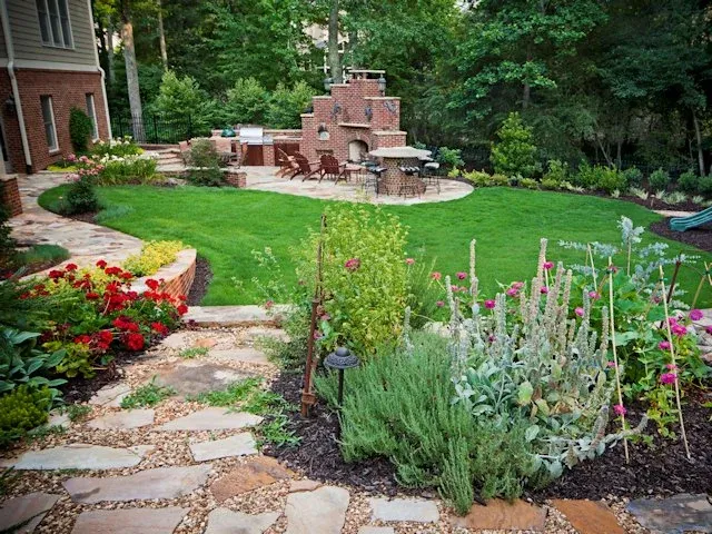 Flower-lined stone path leading across a lawn to a brick outdoor kitchen