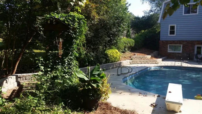 Backyard swimming pool bordered by stone walls and mature trees
