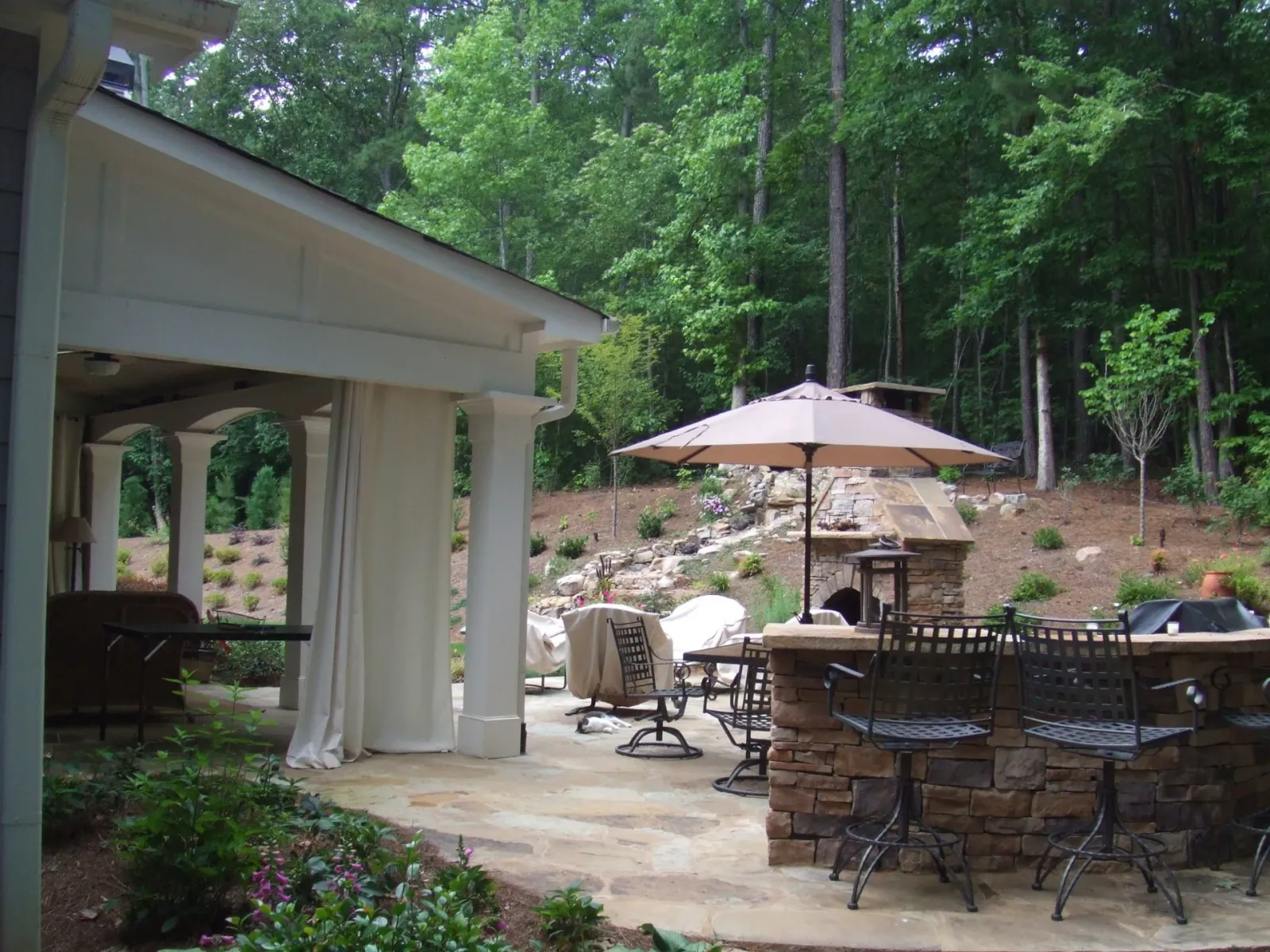 Covered outdoor dining space and stone patio surrounded by a woodland garden