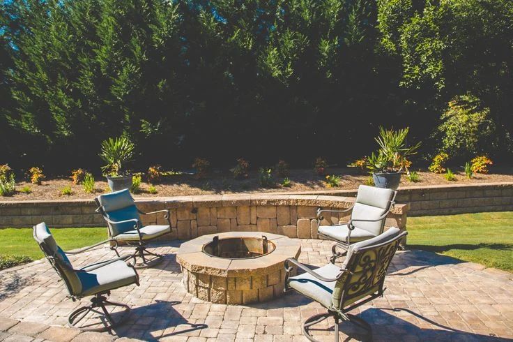 Stone fire pit and lounge chairs beside a curved seating wall and green lawn