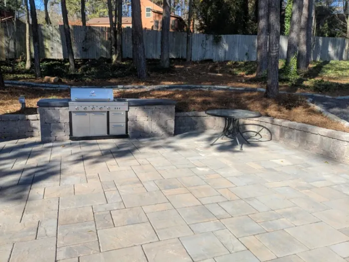 Stone outdoor grill island and paver patio in a wooded backyard