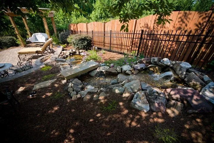Garden pond and natural stone waterfall beside a shaded patio