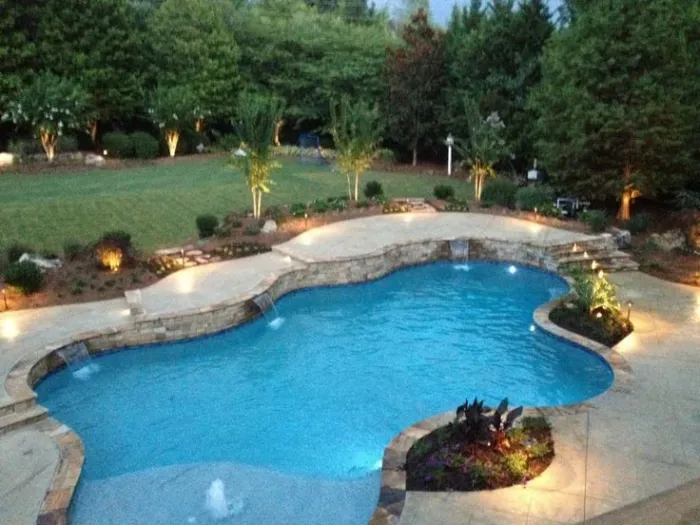 Curved swimming pool with planted beds and landscape lighting