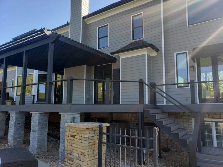 Raised composite deck and pergola with black rails and stone columns