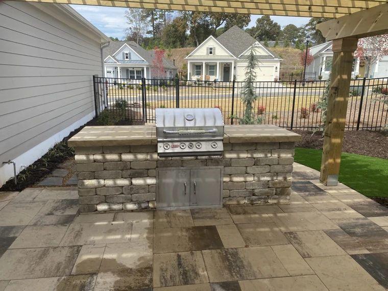 Built-in stainless steel grill and stone kitchen island beneath a pergola