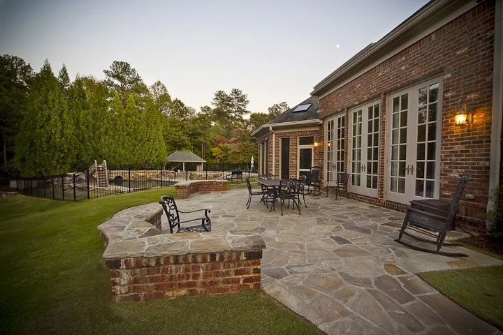 Stone patio with outdoor seating beside a brick home at dusk