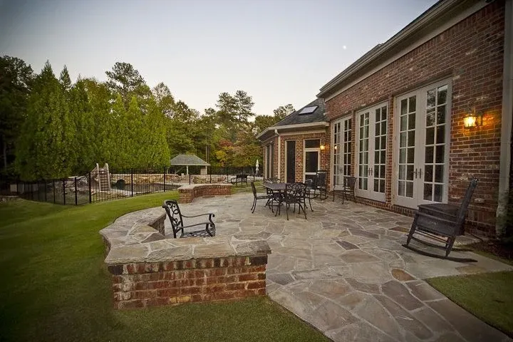 Stone patio with outdoor seating beside a brick home at dusk