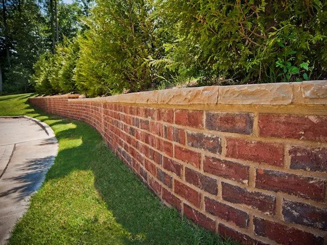 Brick garden wall with a stone cap beside a lawn and walkway