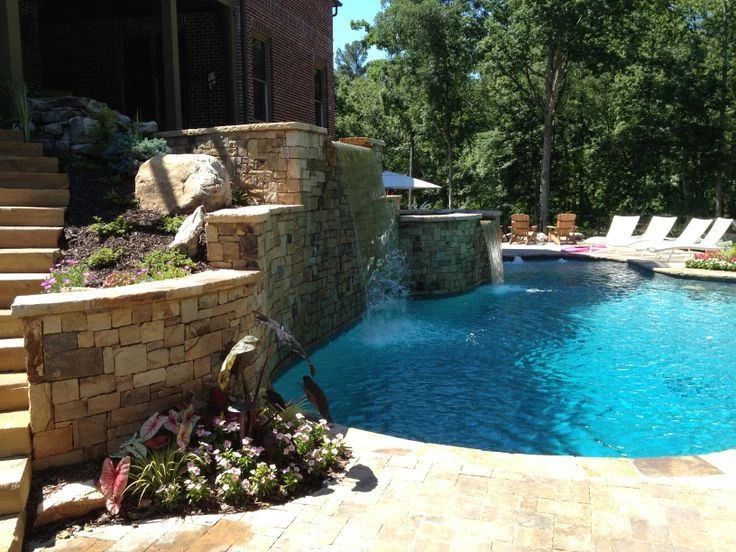 Blue swimming pool with a curved stone waterfall and planted poolside beds