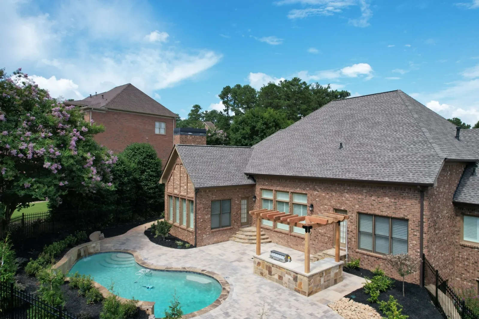 Swimming pool, stone terrace, and outdoor kitchen beside a brick home