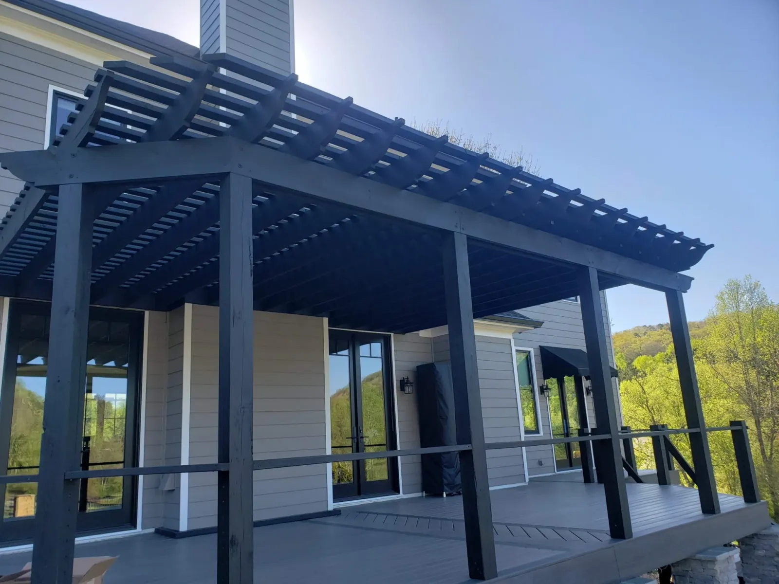 Dark pergola over a finished composite deck with stone columns