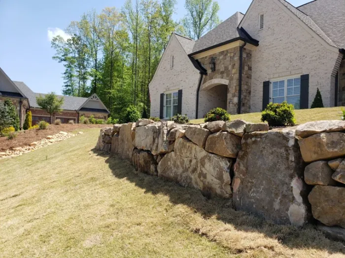 Natural boulder retaining wall supporting a lawn beside a home