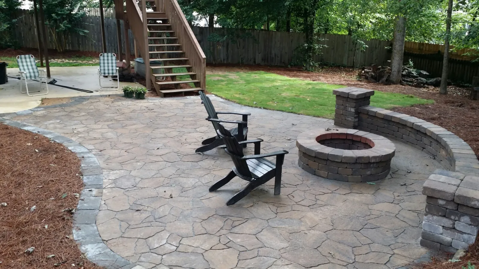 Stone patio with a curved seating wall, fire pit, and broad lawn