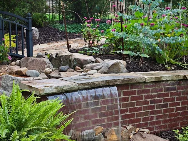 Brick garden water feature with ferns and a planted border