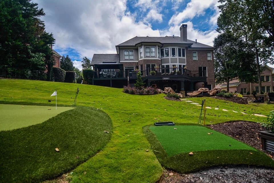 Backyard putting green, lawn, and stone landscaping behind a home