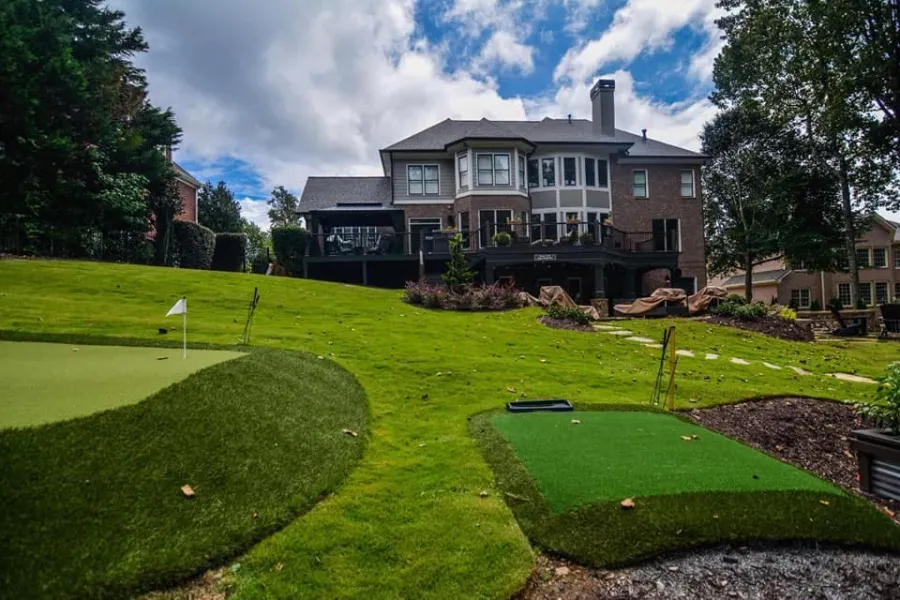 Backyard putting green, lawn, and stone landscaping behind a home