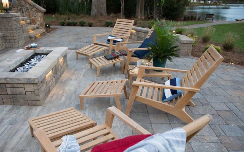 Wood lounge chairs and a stone fire pit on a lakeside patio
