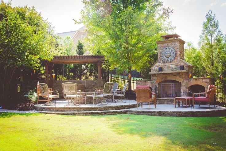 Lawn leading to a curved patio, stone fireplace, and timber pergola