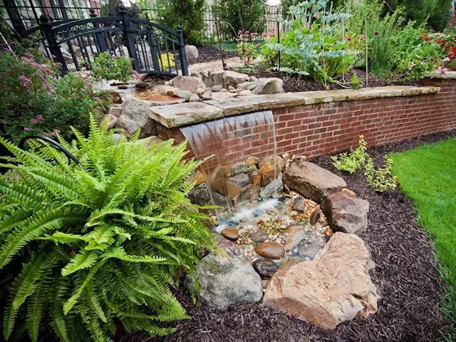 Natural stone waterfall and ferns beside a raised brick garden bed