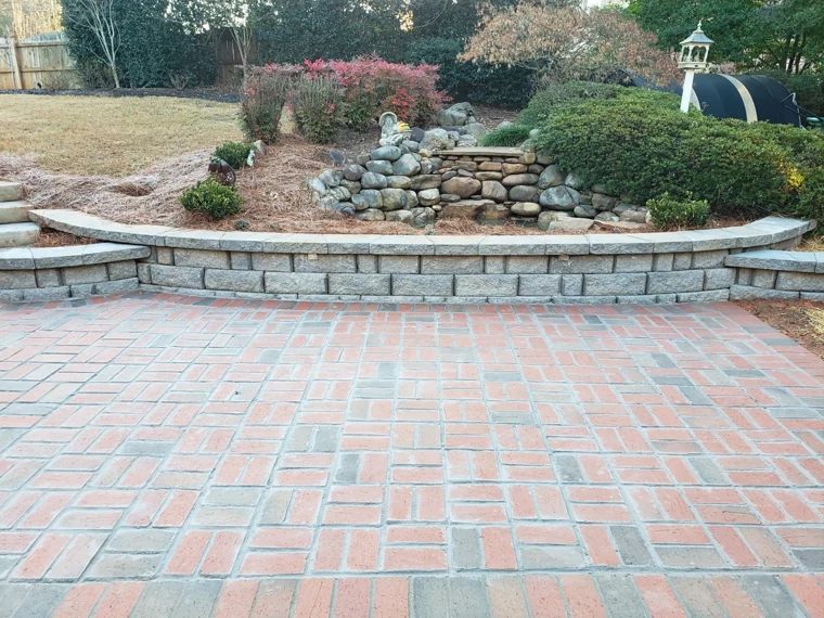 Curved block retaining wall supporting a rock garden beside a paver patio