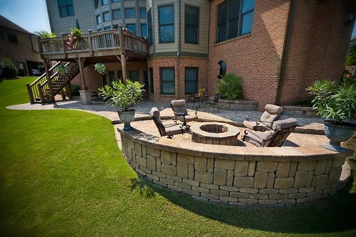 Raised paver patio with a stone fire pit and lounge chairs beside a brick home