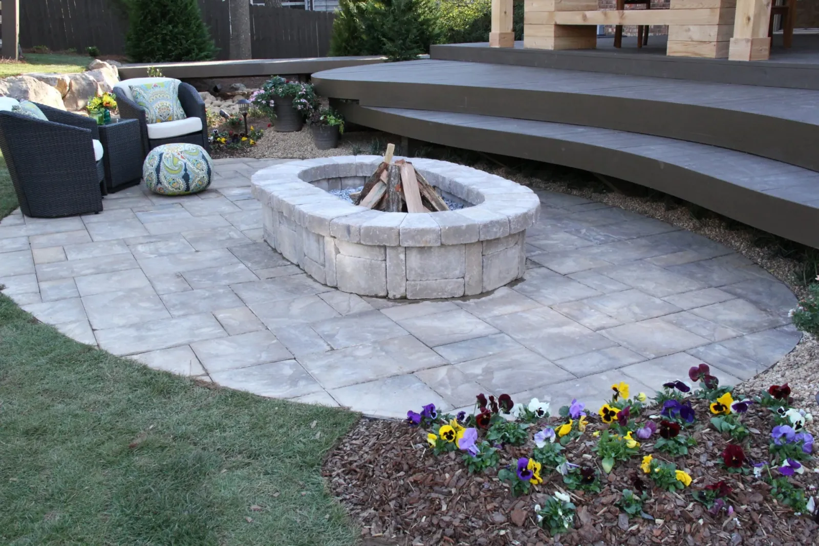 Stone fire pit beside a finished composite deck and colorful garden pots