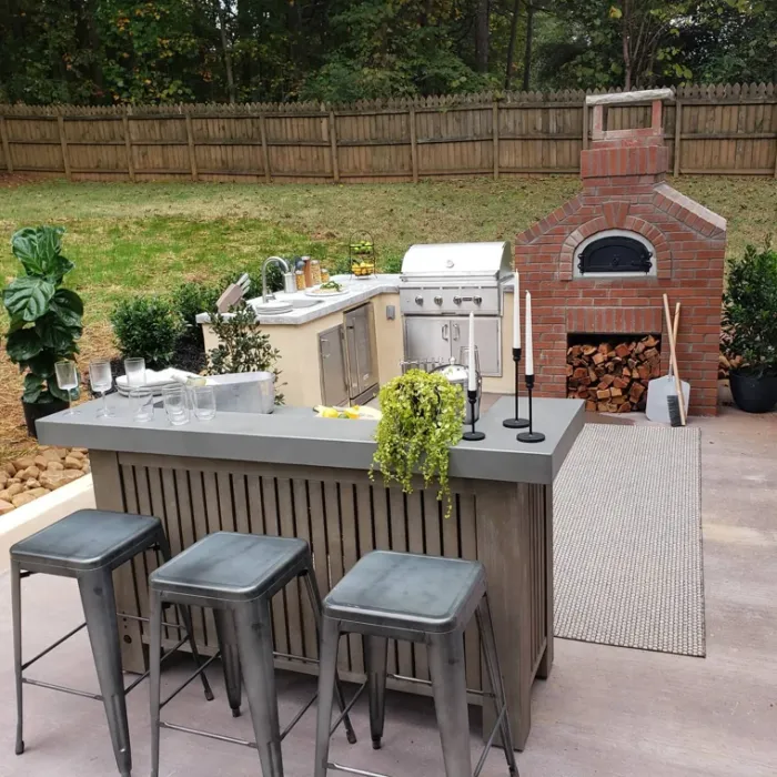Outdoor kitchen with stainless steel grill, pizza oven, and counter seating