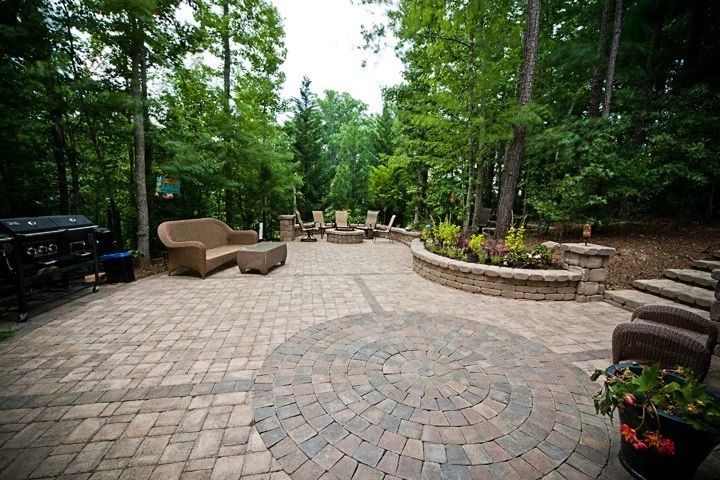 Broad paver patio surrounded by trees, outdoor furniture, and curved planting beds