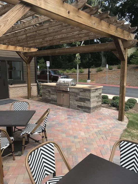 Stone outdoor grill island beneath a timber pergola beside a dining patio