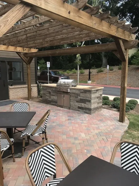 Stone outdoor grill island beneath a timber pergola beside a dining patio